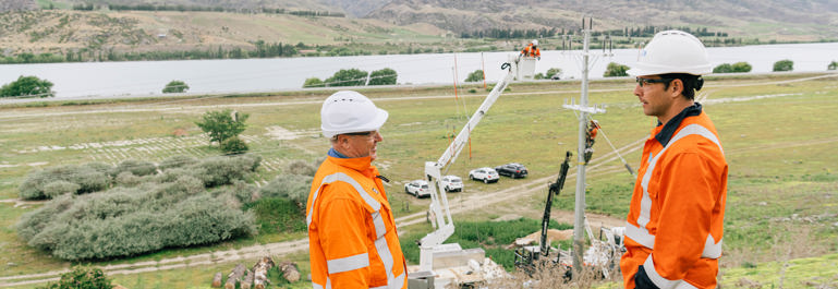 Central Otago, Mark Pratt speaking to someone atop a hill with workers working on the power pole and power lines behind them.