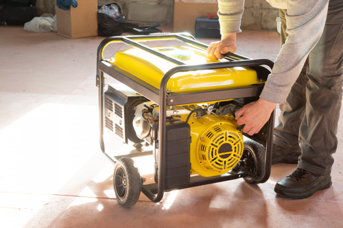 Image of a person leaning over to turn on a yellow and black generator.
