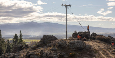 Photo of Earnscleugh Rd lines project, workers standing next to a power pole atop a dusty and rocky hill.