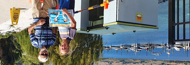 Streetart: Sunny day next to Lake Wakatipu, artist and another person standing in front of a transmission box to be painted. 