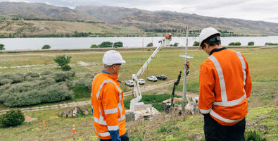 Two people wearing personal protective equipment looking at work on a power pole