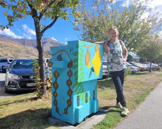 Local artist Chrissy Wikes standing next to transformer with painting of Kowhai