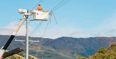 Photo of a worker in a cherry picker basket lifted to the top of a power pole. Power lines haave been clipped together to allow work to progress safely.