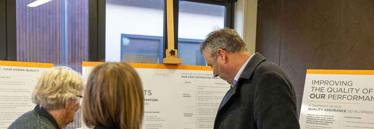 Photo of from a community event. Three people with their backs to the camera are looking at an information board.
