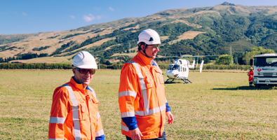 Outram B line helipull project: two workers in PPE gear walking in front of helicopter.