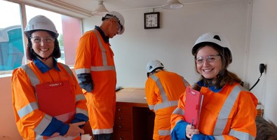 Four people in an office holding clipboards wearing full PPE gear