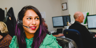 A woman at her office desk wearing a headset, turning away from her desk.