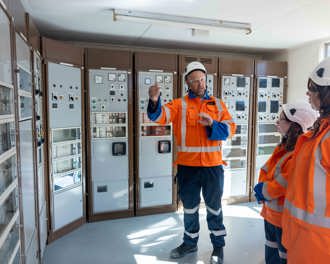 Photo shows a person speaking to two others standing in front of equipment at substation