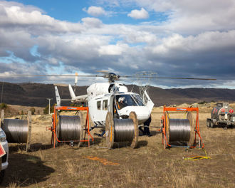 Photo shows a helicopter on the ground with a pilot inside, it sits behind for large coils of power lines as part of the Earnscleugh Rd lines project