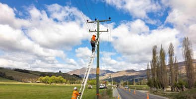 Workers on a ladder against a power pole working in a rural setting