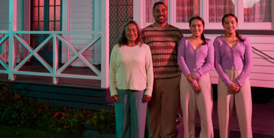 Photo of a family of four people: mother, father and twin teenaged girls standing in front of their home with a pink light filter 
