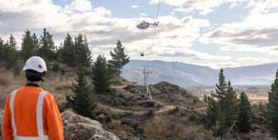 Helicopter bringing a large power line reel in to Earnscleugh Rd with a worker watching on in the foreground