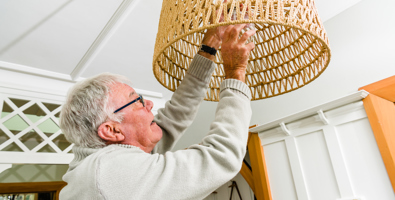 Photo of an older man reaching up to change a lightbulb.