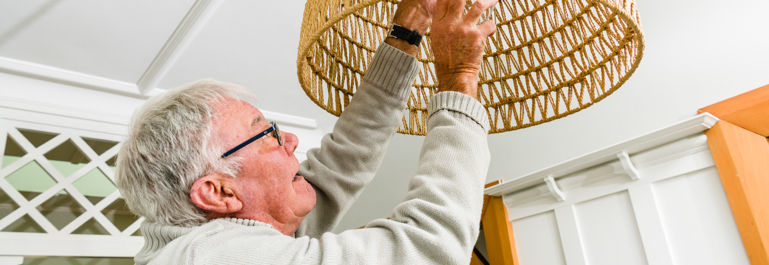 Photo of an older man reaching up to change a lightbulb.