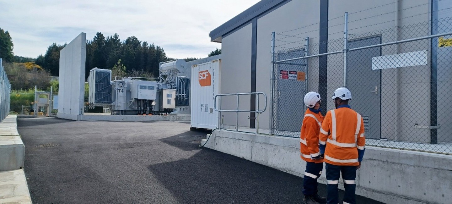 Two people in orange personal protection clothing standing in front of the new Green Island Zone Subsation building