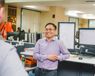 A man standing in front of his desk smiling.