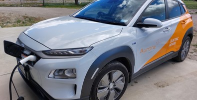 Aurora Energy branded electric car shown plugged in to a charger.