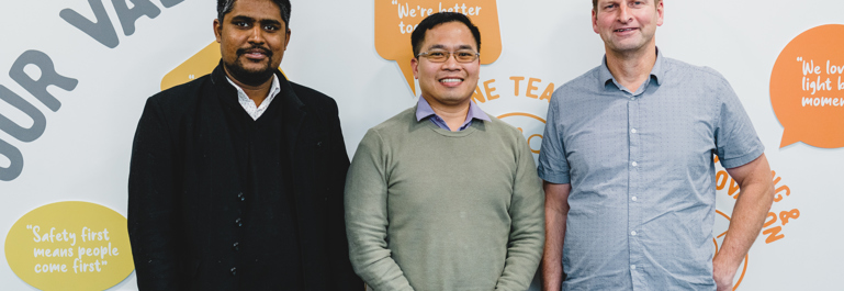 Three men standing in front of a wall that explains Aurora Energy's values