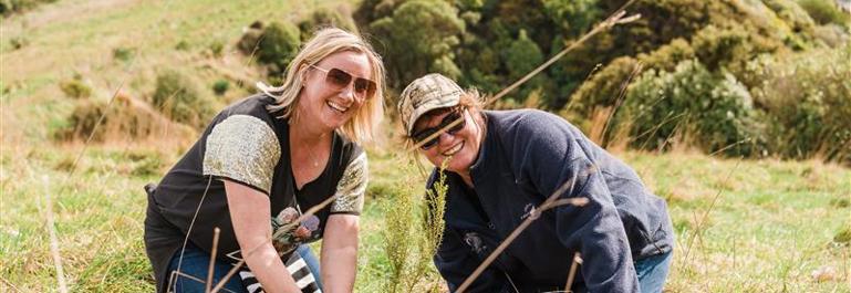 Aurora Energy Planting Day, two women kneeling down planting natives trees.
