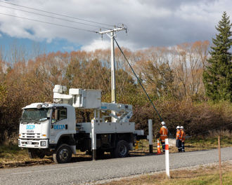 Photo shows a Delta truck with its cherry picker lowered, three workers in PPE are standing next to a power pole