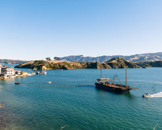 Large boat heading across Otago Harbour, laying submarine cable on a sunny day with Marine Science Centre in the background