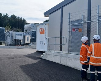 Two people in orange personal protection clothing standing outside the new switching room building.