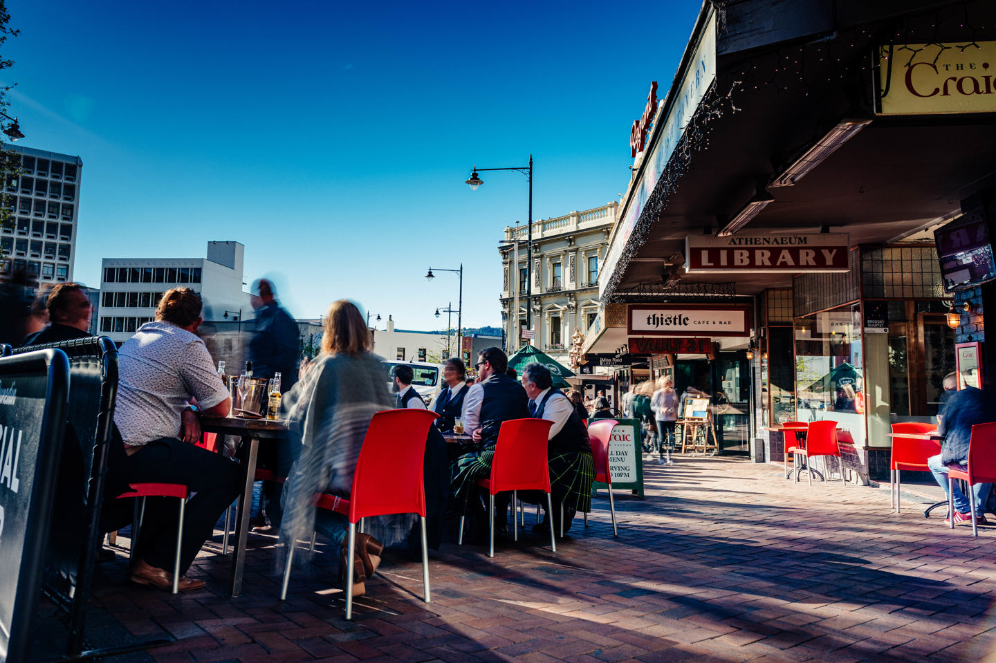 Photo of people sitting outside a restaurant in The Octagon, Dunedin with blue skies in the background.