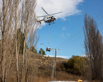 Photo shows a helicopter lowering coil of pwer lines next to a power line as part of the Earnscleugh Rd lines project