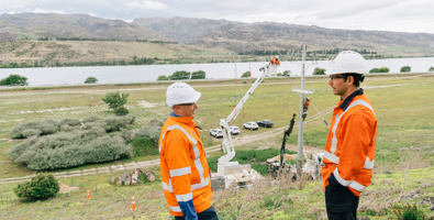 Central Otago, Mark Pratt speaking to someone atop a hill with workers working on the power pole and power lines behind them.