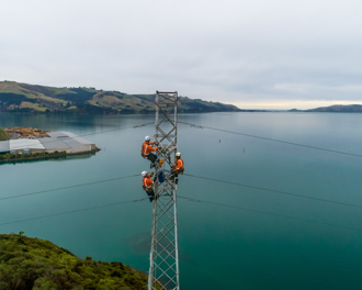 Three workers on a tower with Otago Harbour in the background