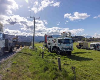 Photo shows Delta utility trucks and utes parked in a paddock and on the side of a road next to a power pole